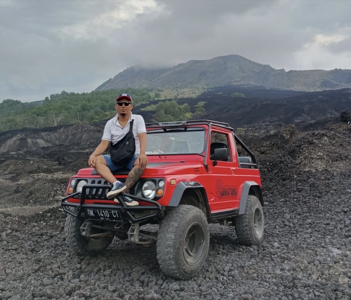 Ajik sitting on a red jeep near Mount Batur in Bali